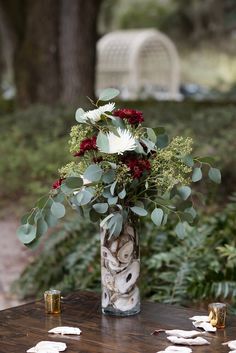 a vase filled with flowers sitting on top of a wooden table next to a forest