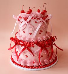 three tiered cake with hearts and bows on top, sitting on a pink surface