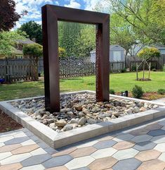 a large metal sculpture sitting on top of a stone floor next to a lush green yard