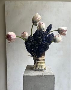 a vase filled with lots of flowers on top of a cement block in front of a white wall