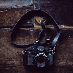 a camera sitting on top of a wooden table next to a black strap with the word nikon printed on it