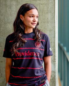 a woman standing in front of a wall wearing a black shirt with red writing on it