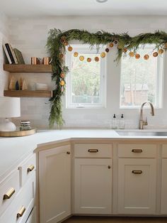 a kitchen decorated for christmas with garland on the window sill and lights hanging over the sink