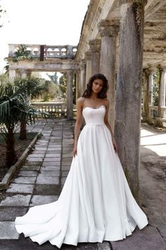 a woman in a white wedding dress leaning against a pillar with her hands on her hips