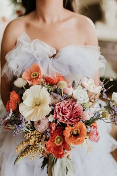 a woman holding a bouquet of flowers in her hands and wearing a white wedding dress