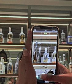 a person holding up a cell phone in front of shelves with liquor bottles on them