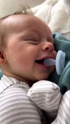 a baby laying on top of a bed with a pacifier in its mouth and smiling