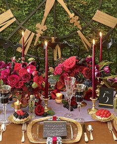 the table is set with candles, plates and flowers in red and pink colors on it