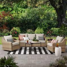 an outdoor living room with wicker furniture and striped rugs on the floor, surrounded by greenery