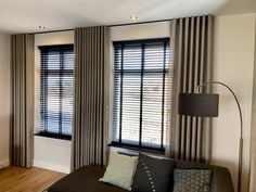 a living room filled with furniture and large windows covered in shades of grey blinds on top of them