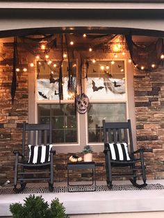 two rocking chairs sitting on the front porch with halloween decorations and lights hanging from the windows