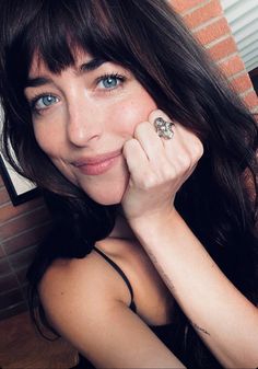 a close up of a person with a ring on her finger and brick wall in the background