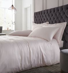 a bed with white sheets and pillows next to a gray upholstered headboard