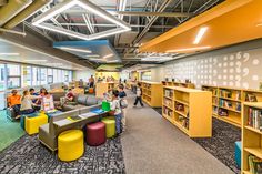 people are sitting and standing in the open area of an office building with yellow bookshelves