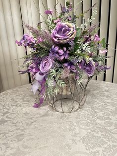 a vase filled with purple flowers sitting on top of a white tablecloth covered table