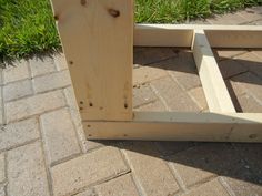 a wooden bench sitting on top of a brick floor next to green grass and bushes