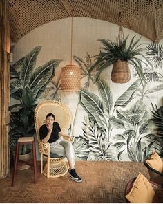 a man sitting in a wicker chair next to a wall with plants on it