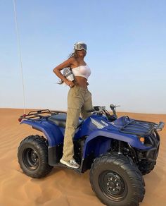 a woman standing on top of a blue four wheeler in the middle of the desert