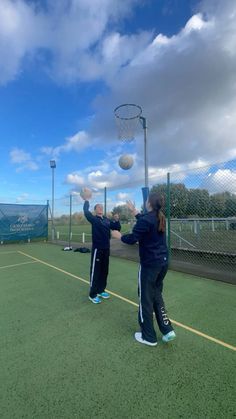 two girls playing basketball on an outdoor court with blue skies and clouds in the background