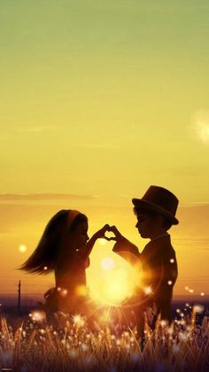 two people are sitting in the grass making a heart shape with their hands at sunset