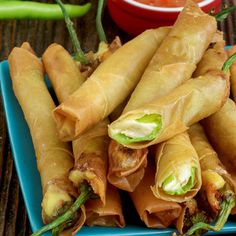 several spring rolls on a blue plate with dipping sauce and green peppers in the background