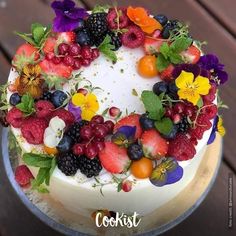 a white cake topped with fruit and flowers on top of a wooden table next to a plate