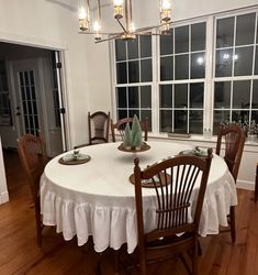 a dining room table with chairs and a white table cloth on it in front of large windows