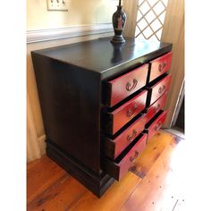 a red and black dresser sitting on top of a wooden floor next to a lamp