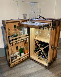 an open wooden cabinet with wine glasses and bottles in it on the floor next to a wall