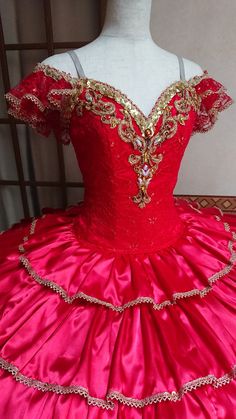 a red ball gown with gold trimmings on the bustle and shoulders, in front of a mannequin