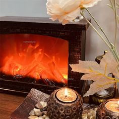 two candles sitting next to each other on a table with flowers in front of the fireplace