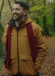 a man and woman standing in the woods smiling at each other's side with trees behind them