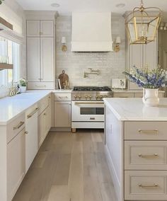 a large kitchen with white cabinets and wood flooring is pictured in this image, there are flowers on the countertop