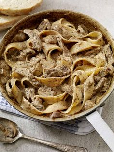 a pan filled with pasta and meat on top of a table next to slices of bread