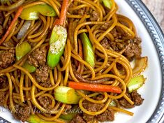 a white plate topped with noodles and meat on top of a wooden table next to a fork