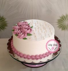 a white and pink cake with flowers on the top is sitting on a glass platter