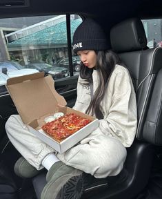 a woman sitting in the back seat of a car with a pizza box on her lap