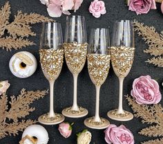 four wine glasses with gold glitter on them sitting next to pink flowers and doughnuts