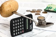 a small calculator sitting on top of a pile of money next to a potato