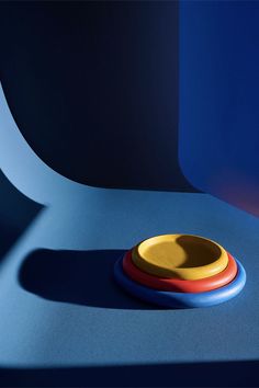 a yellow and red bowl sitting on top of a blue table next to a black wall