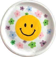 a white plate with a smiley face painted on the side and flowers all around it