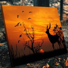 a deer is silhouetted against an orange sunset with birds flying in the sky above it