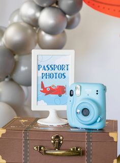 a blue camera sitting on top of a suitcase next to a sign that says passport photos