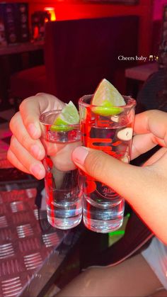 two people holding up glasses with limes and vodka on the table in front of them