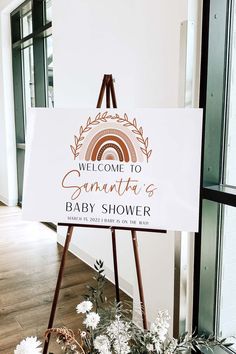 a welcome sign for a baby shower with flowers in the foreground and an easel next to it