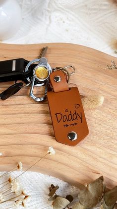 a leather keychain with the word daddy written on it sitting next to a pair of scissors