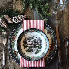 a christmas place setting on a wooden table with pine cones and napkins, silverware and utensils