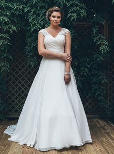 a woman in a wedding dress standing on a wooden floor with greenery behind her