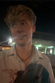 a young man wearing a shirt and necklace standing in front of a building at night