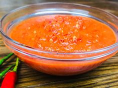 a glass bowl filled with red sauce next to two chili peppers on a wooden table